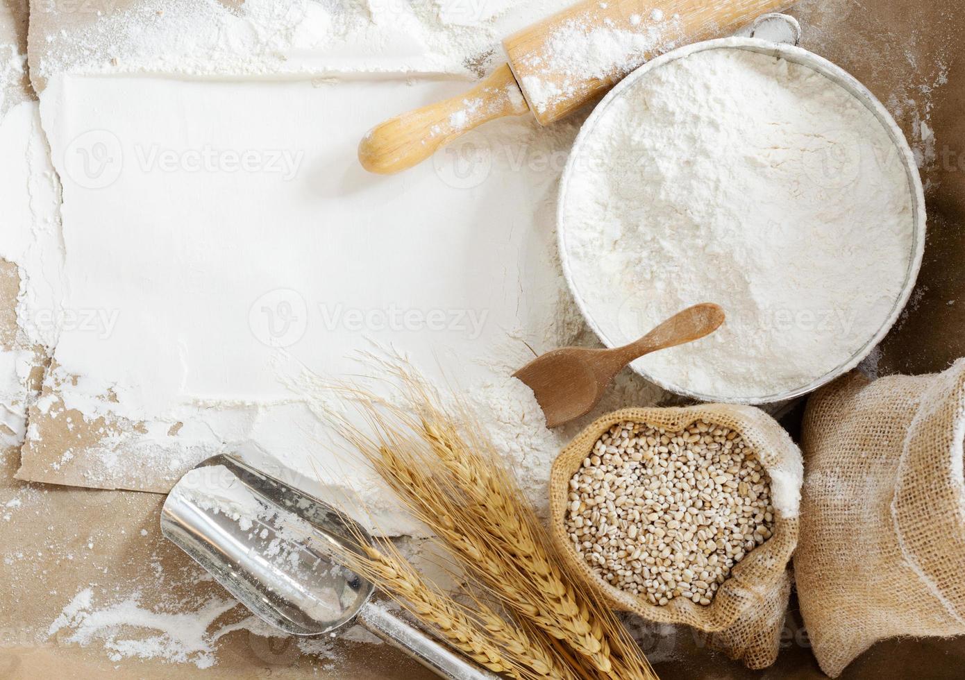 Flour in a bowl and wheat grains with wheat ears on the table, paper background In a rustic kitchen, top view photo