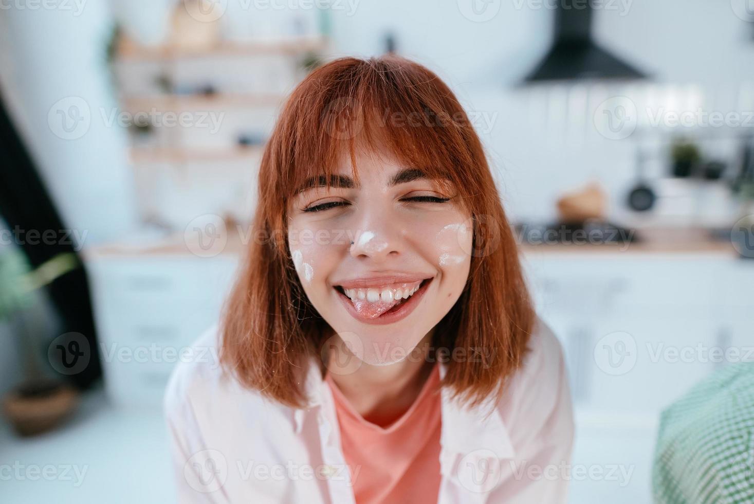 Playful young woman with flavor on face on the kitchen photo