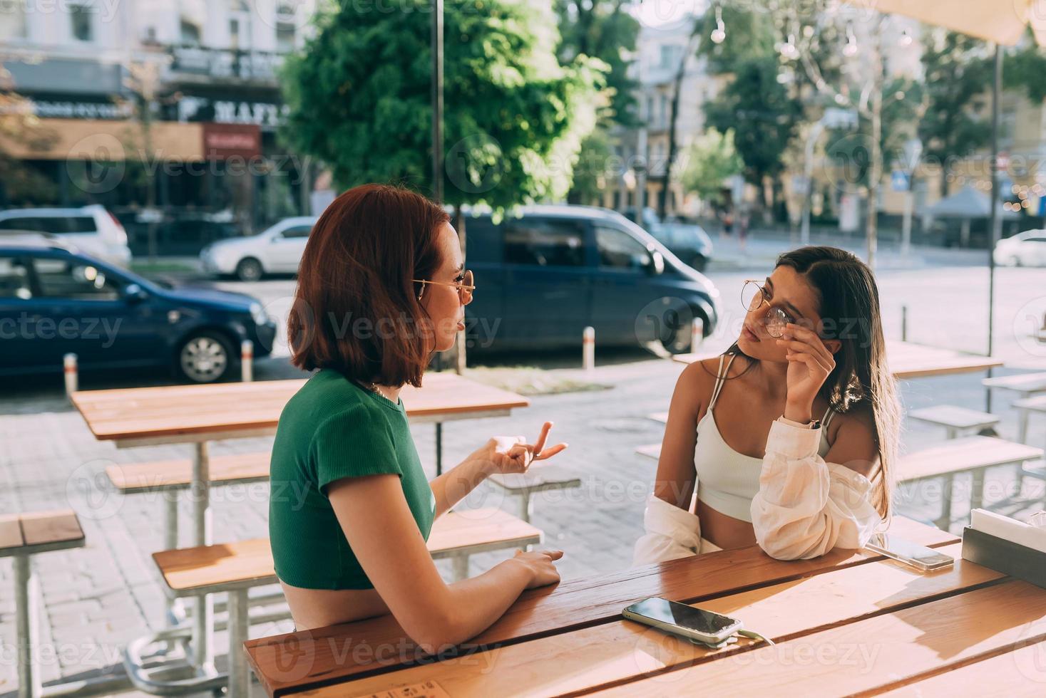 Two pretty girlfriends talking while sitting in a bar outdoors photo