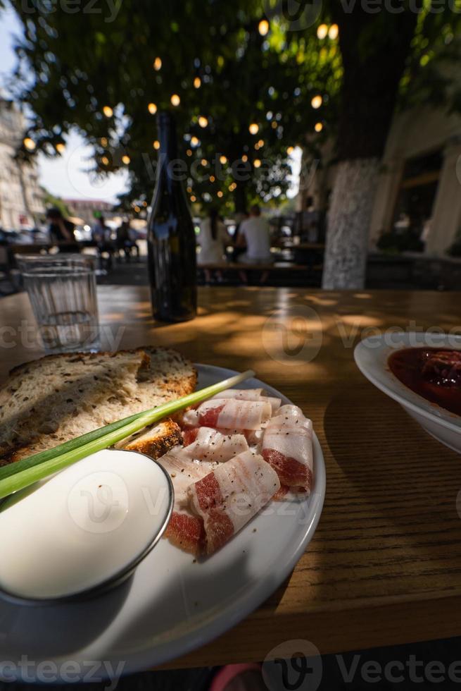 Close up view slices of smoked bacon meat with rye whole grain black bread, green onion and sour cream on the table. photo