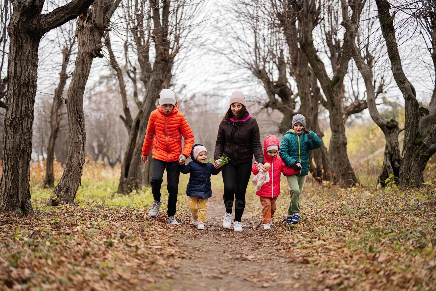 Mother holding hands with her kids running in autumn forest. photo