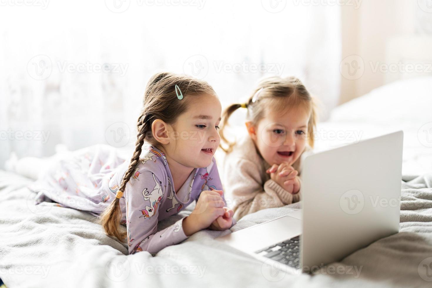 dos muchachas hermanas acecho en ordenador portátil. tecnología y hogar concepto. foto