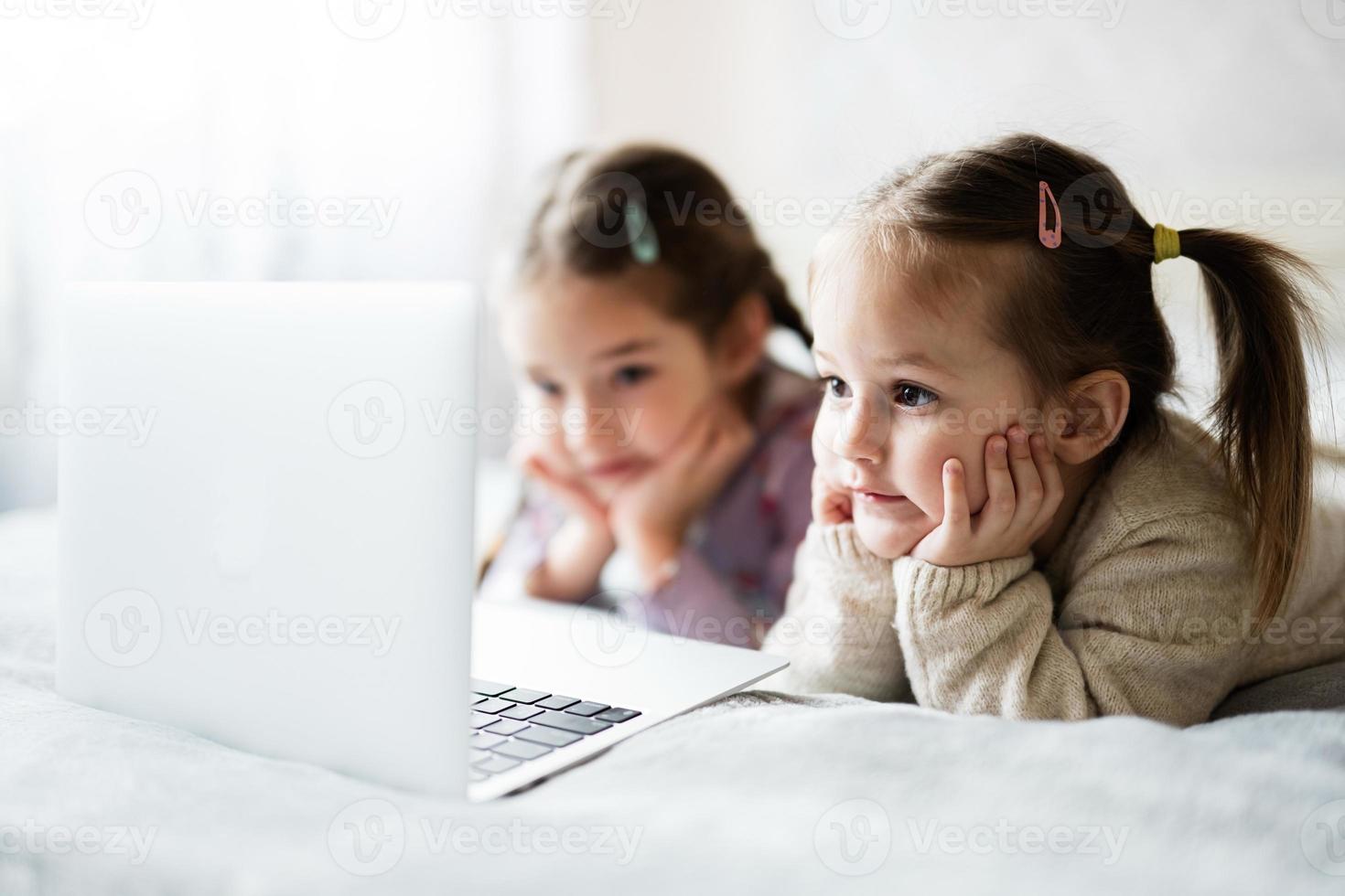 dos muchachas hermanas acecho en ordenador portátil. tecnología y hogar concepto. foto