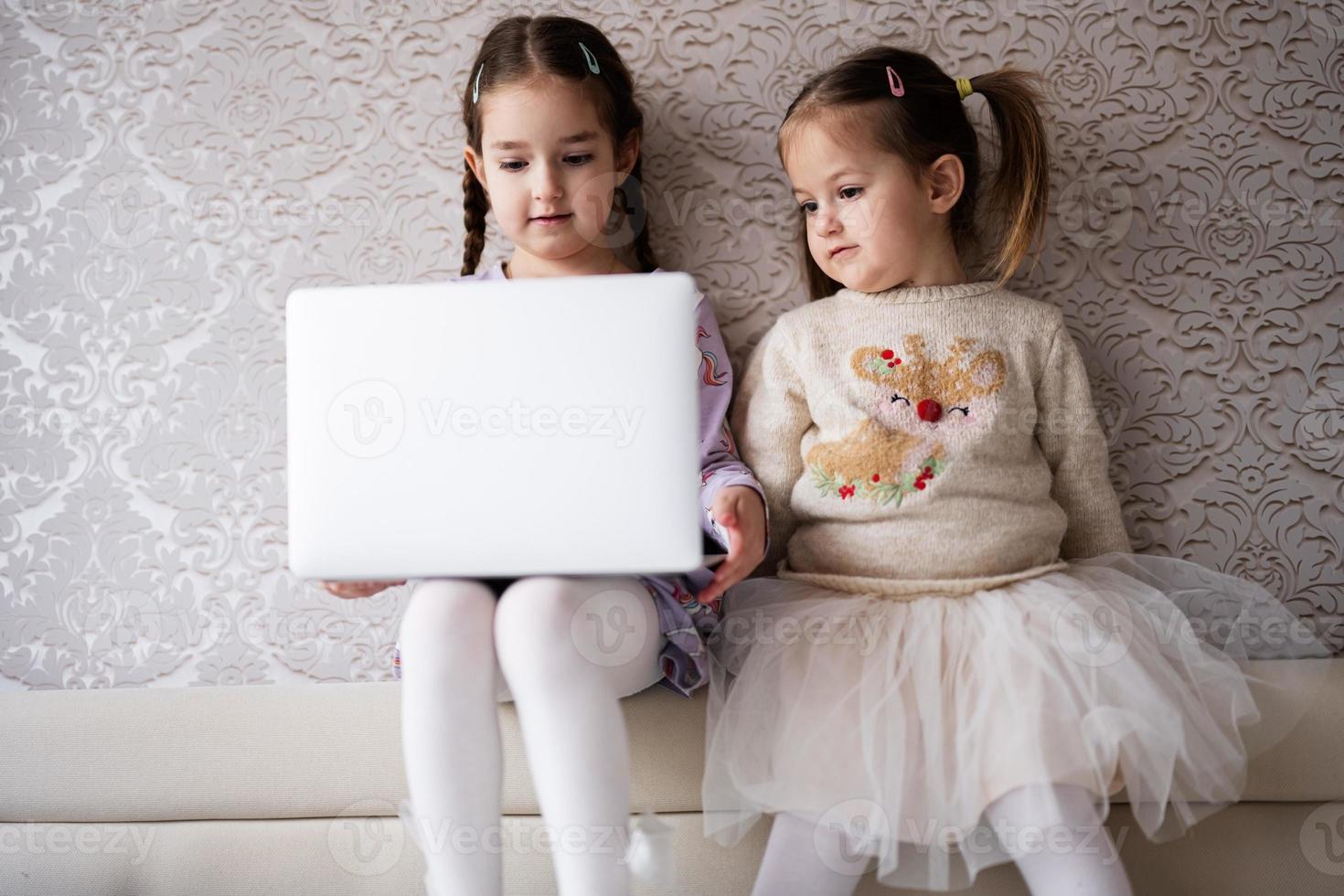 dos muchachas hermanas acecho en ordenador portátil. tecnología y hogar concepto. foto