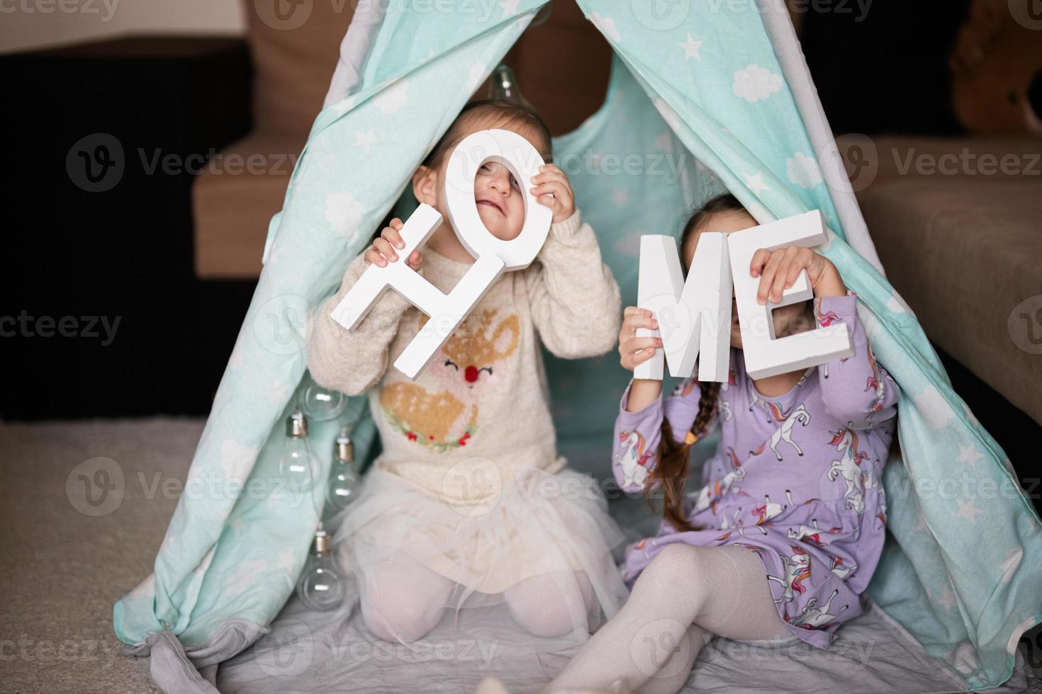 Two girls sisters at wigwam tent with wooden home letters. photo