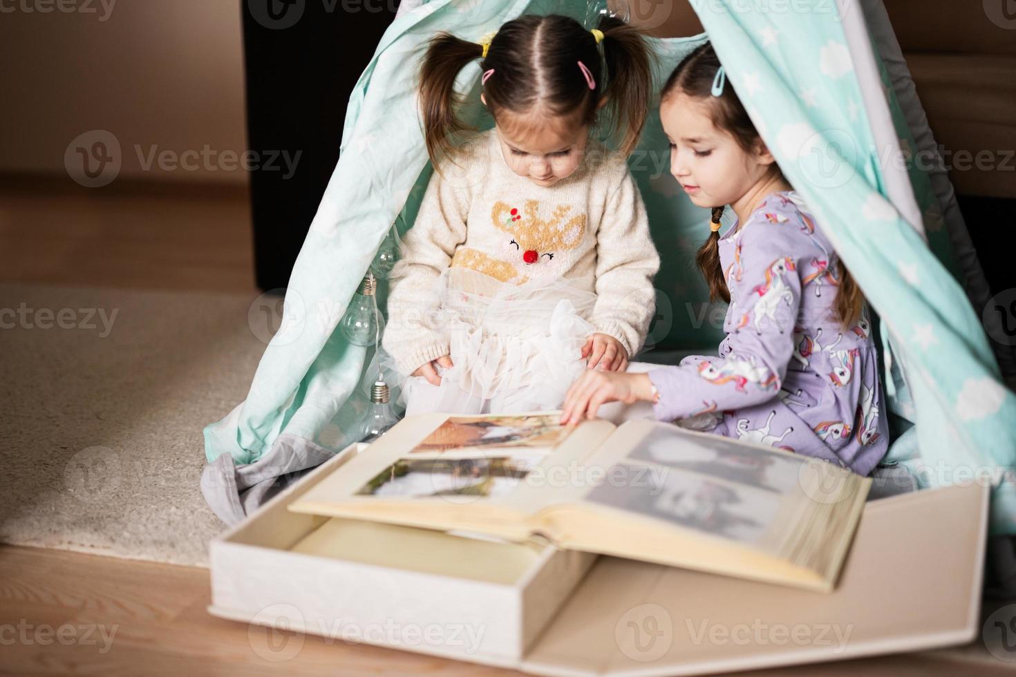Two girls sisters at wigwam tent looking at parents wedding album. photo