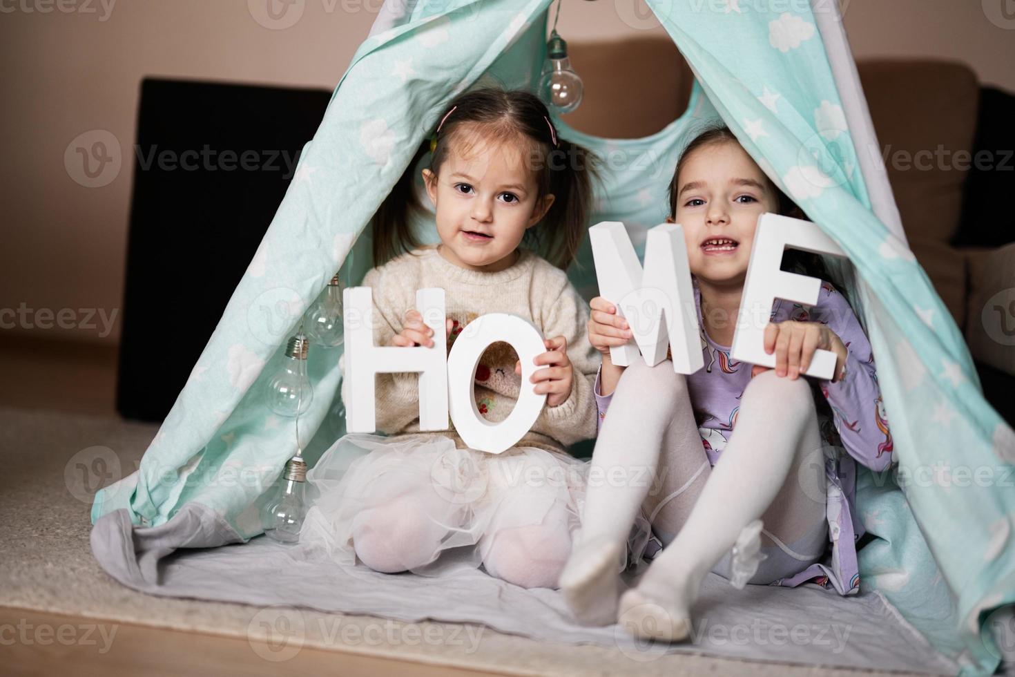 Two girls sisters at wigwam tent with wooden home letters. photo