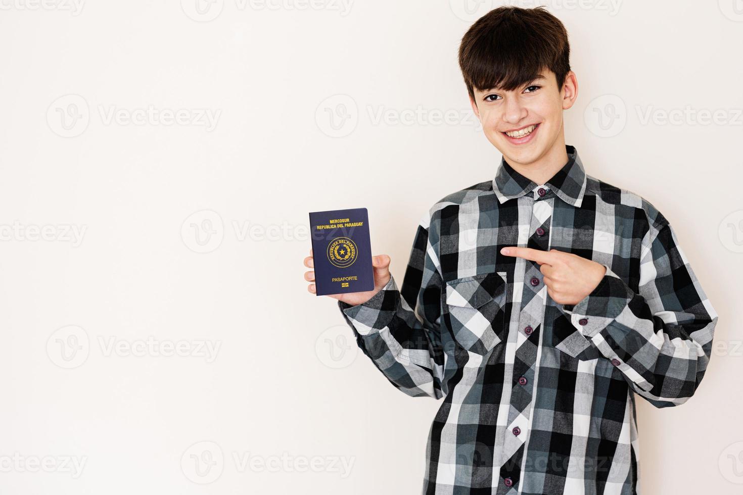 joven adolescente chico participación paraguay pasaporte mirando positivo y contento en pie y sonriente con un confidente sonrisa en contra blanco antecedentes. foto