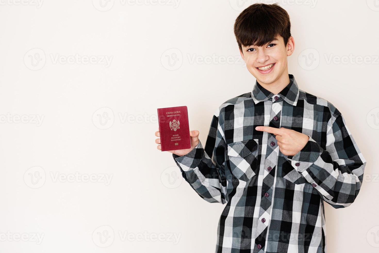 joven adolescente chico participación montenegro pasaporte mirando positivo y contento en pie y sonriente con un confidente sonrisa en contra blanco antecedentes. foto