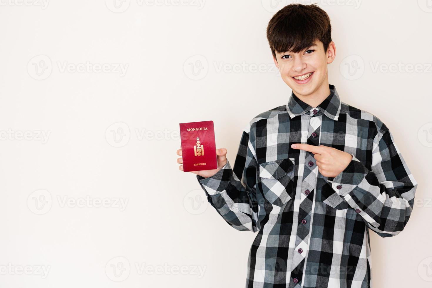 joven adolescente chico participación Mongolia pasaporte mirando positivo y contento en pie y sonriente con un confidente sonrisa en contra blanco antecedentes. foto