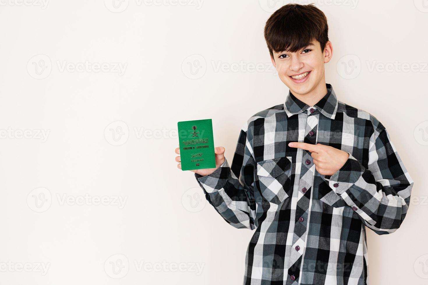 joven adolescente chico participación saudi arabia pasaporte mirando positivo y contento en pie y sonriente con un confidente sonrisa en contra blanco antecedentes. foto