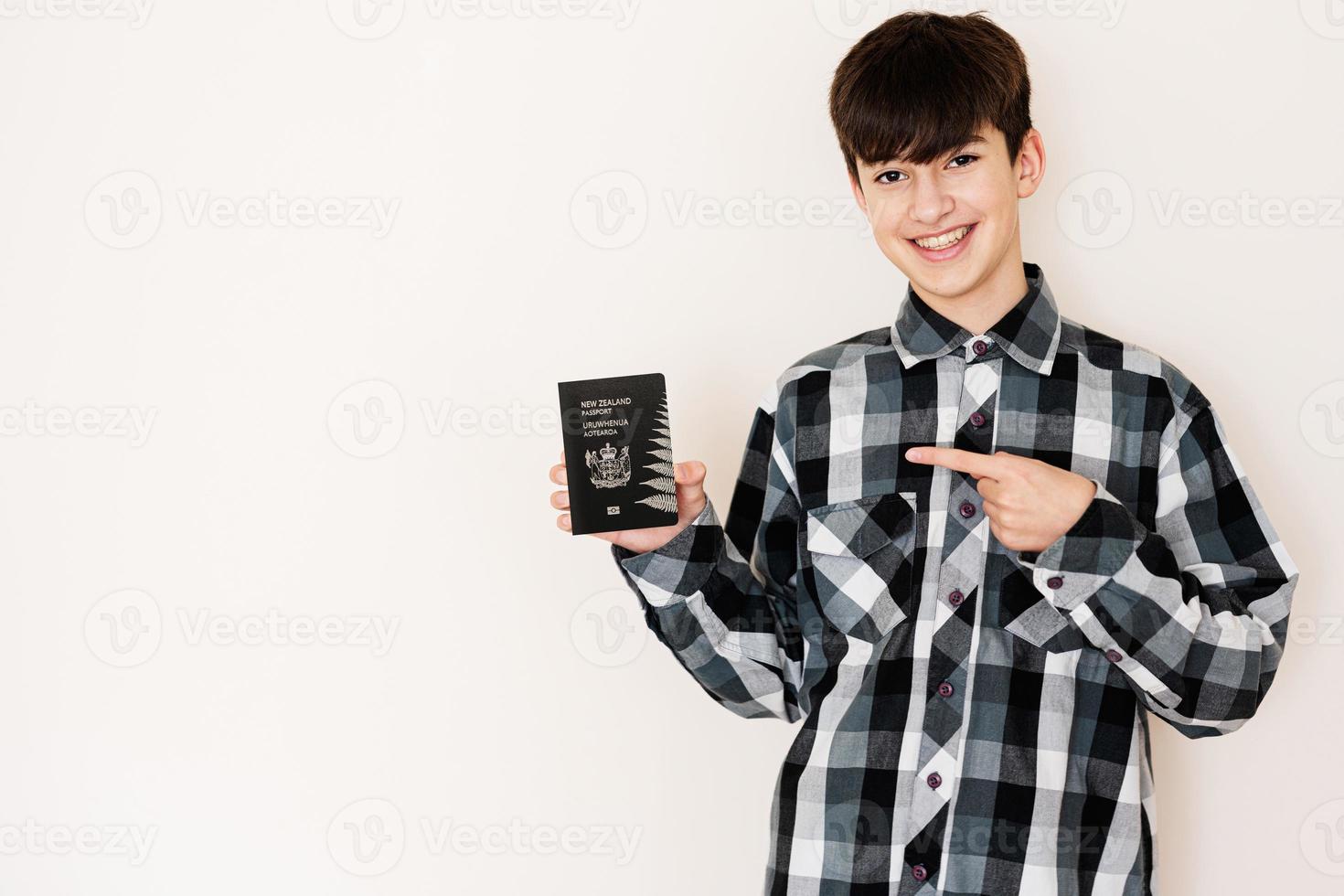 joven adolescente chico participación nuevo Zelanda pasaporte mirando positivo y contento en pie y sonriente con un confidente sonrisa en contra blanco antecedentes. foto