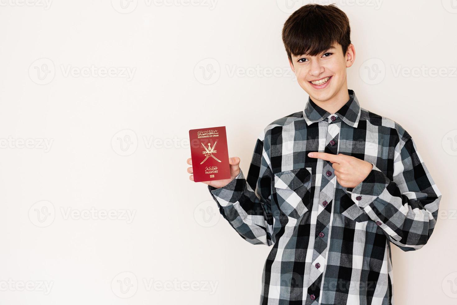 joven adolescente chico participación Omán pasaporte mirando positivo y contento en pie y sonriente con un confidente sonrisa en contra blanco antecedentes. foto