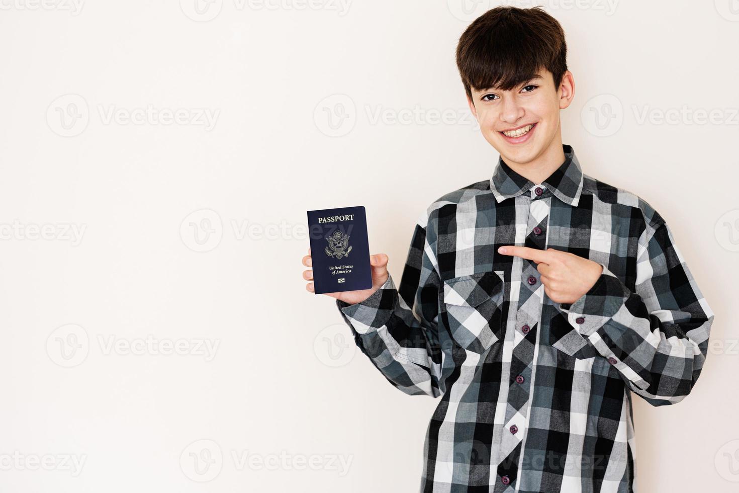 joven adolescente chico participación unido estados de America pasaporte mirando positivo y contento en pie y sonriente con un confidente sonrisa en contra blanco antecedentes. foto