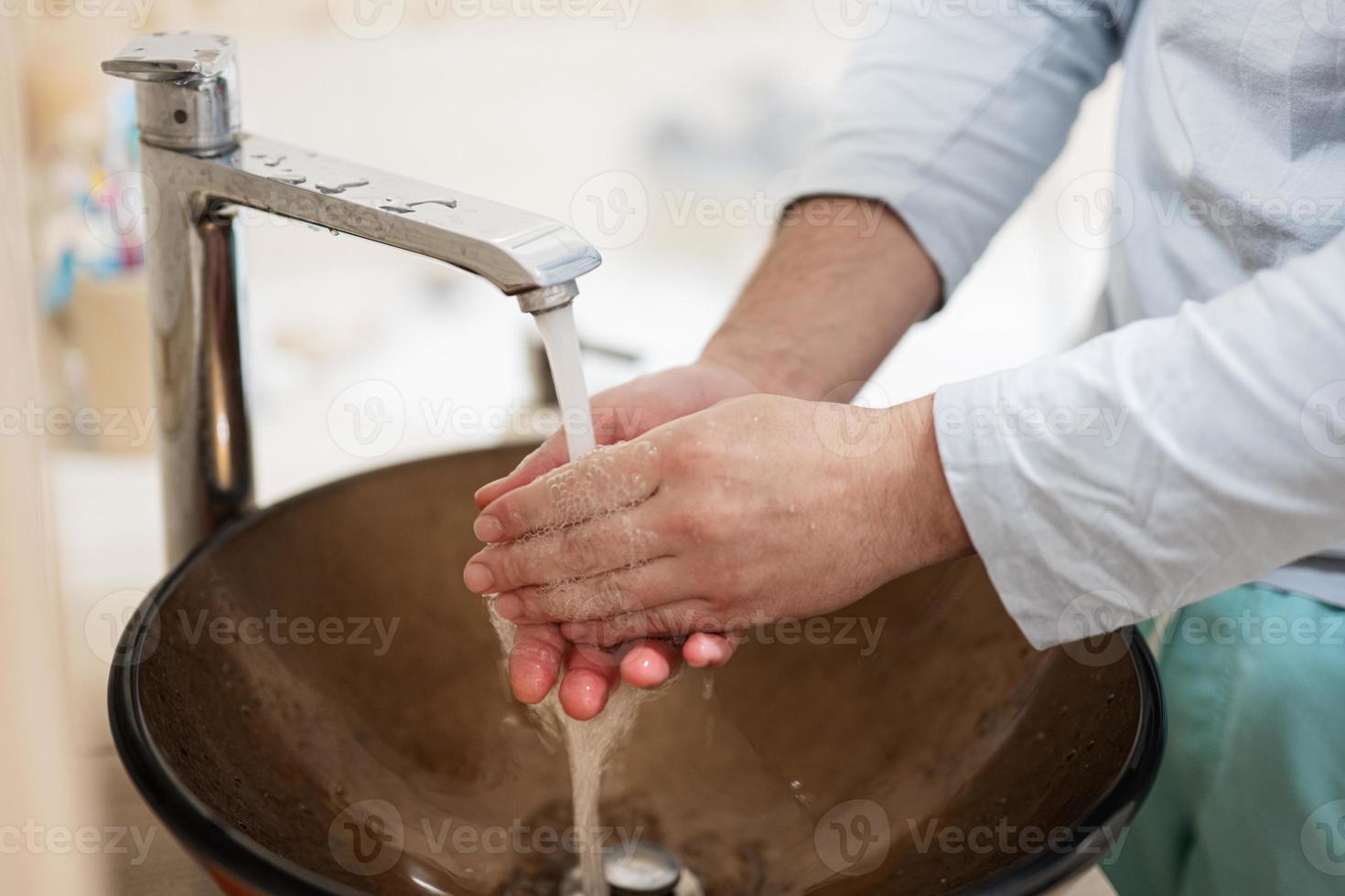 Man washing hands at brown glass hand wash basin with chrome water tap. photo
