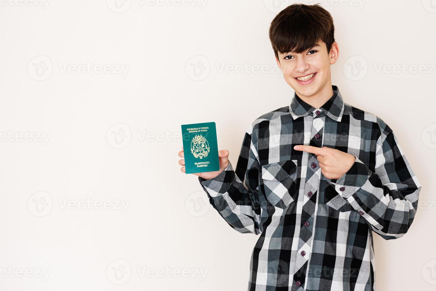 joven adolescente chico participación tonga pasaporte mirando positivo y contento en pie y sonriente con un confidente sonrisa en contra blanco antecedentes. foto