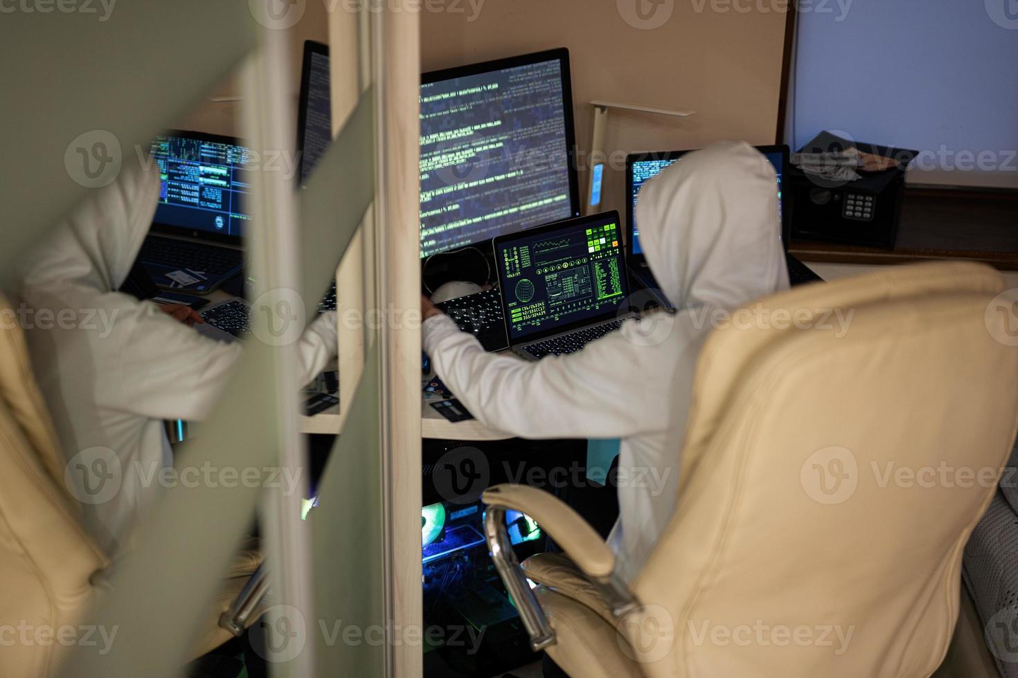 Boy hacker fraudulently use credit card for payment. Internet theft . Man wearing a balaclava and holding a credit card while sat behind a laptop. photo