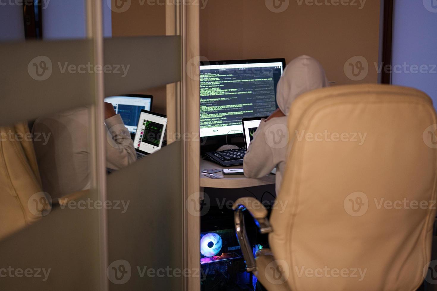 Boy hacker fraudulently use credit card for payment. Internet theft . Man wearing a balaclava and holding a credit card while sat behind a laptop. photo