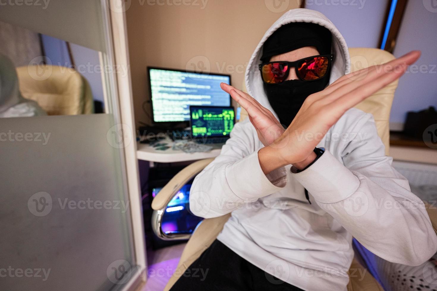 Boy hacker fraudulently use credit card for payment. Internet theft shows cross hands . Man wearing a balaclava and holding a credit card while sat behind a laptop. photo