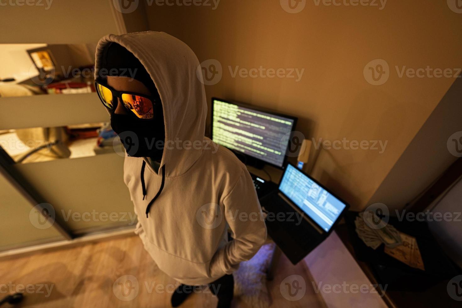 Boy hacker. Internet theft . Man wearing a balaclava behind a laptop. photo