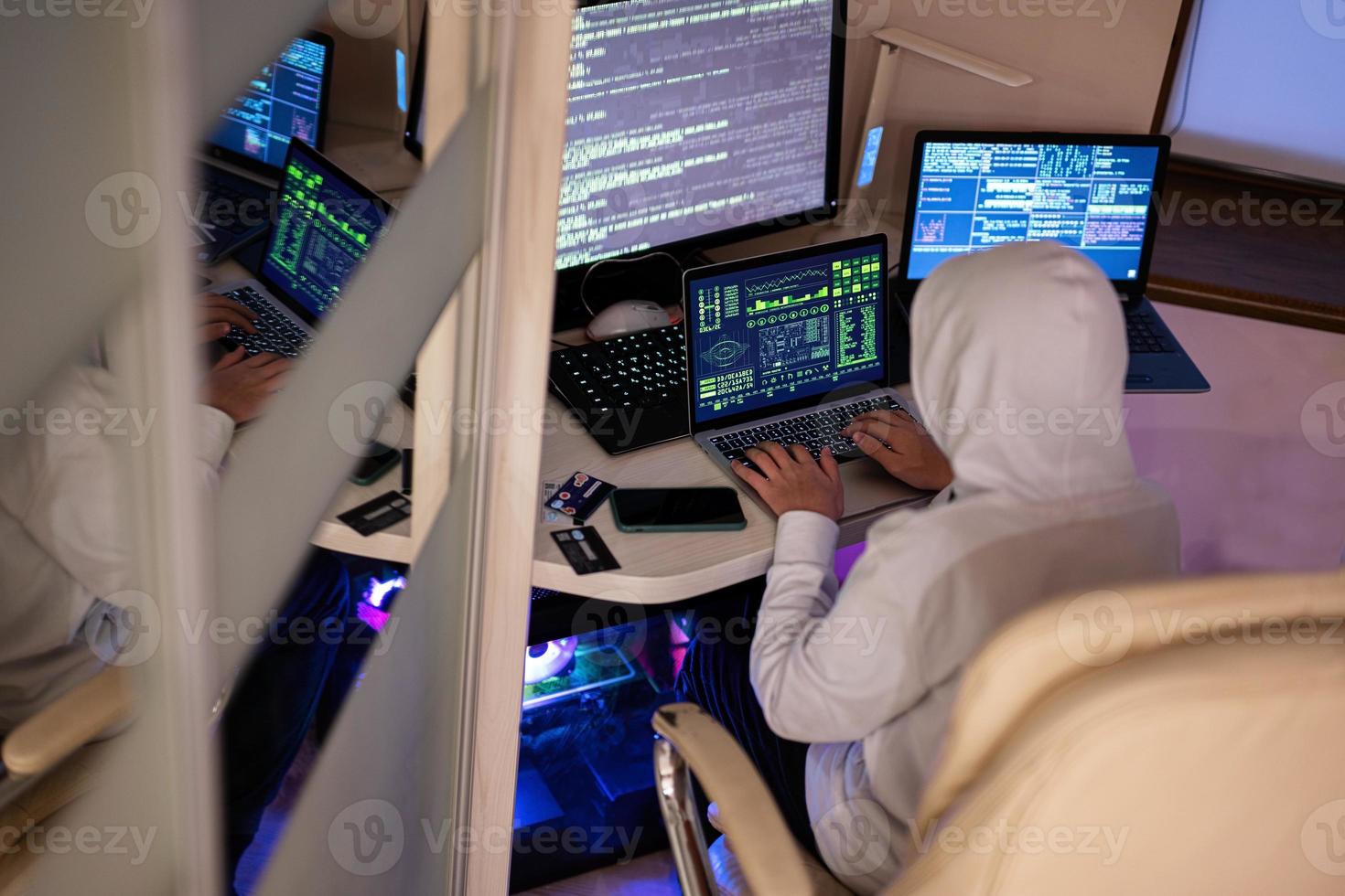 Boy hacker fraudulently use credit card for payment. Internet theft . Man wearing a balaclava and holding a credit card while sat behind a laptop. photo