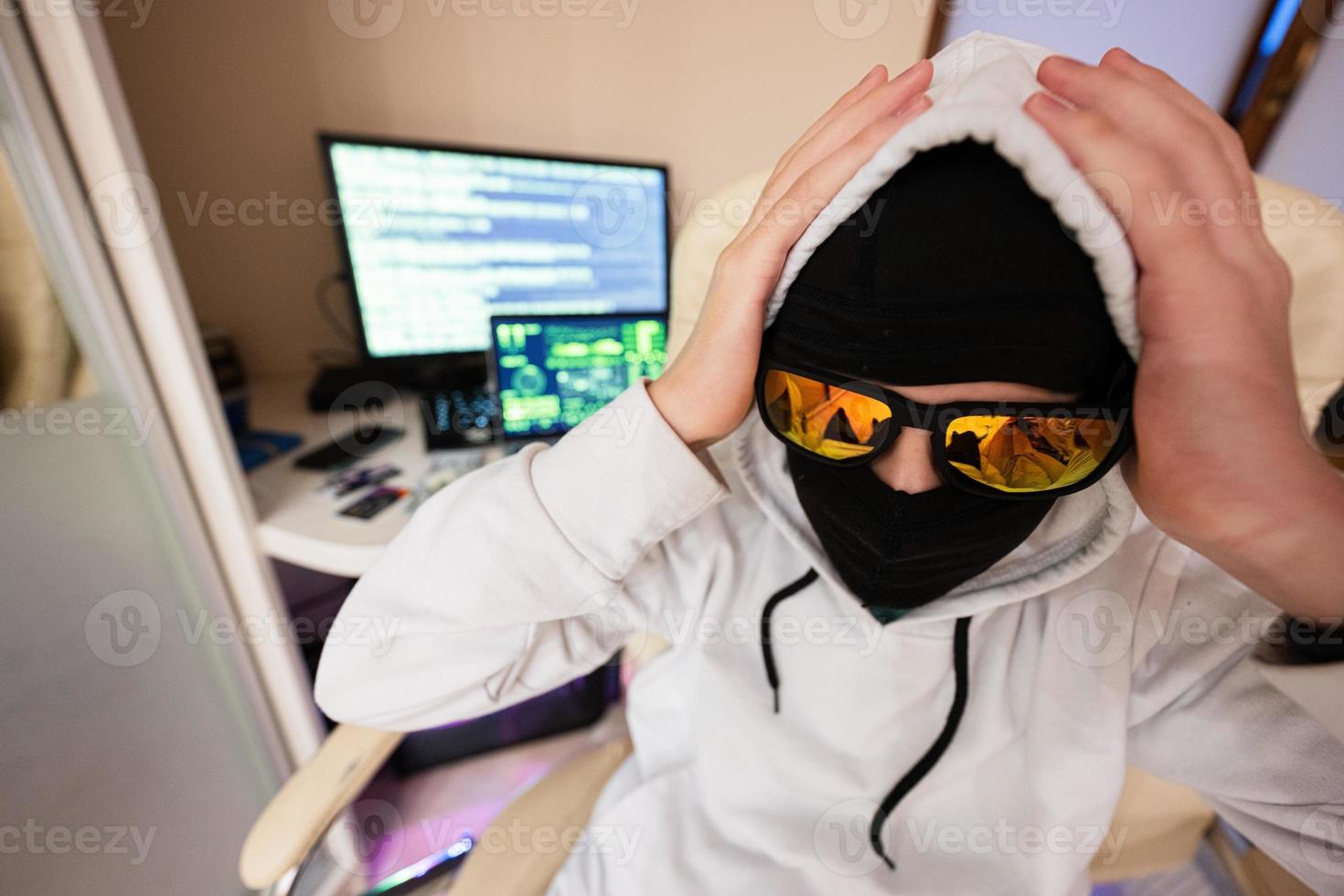 Boy hacker grabbed his head. Internet theft . Man wearing a balaclava sat behind a laptop. photo