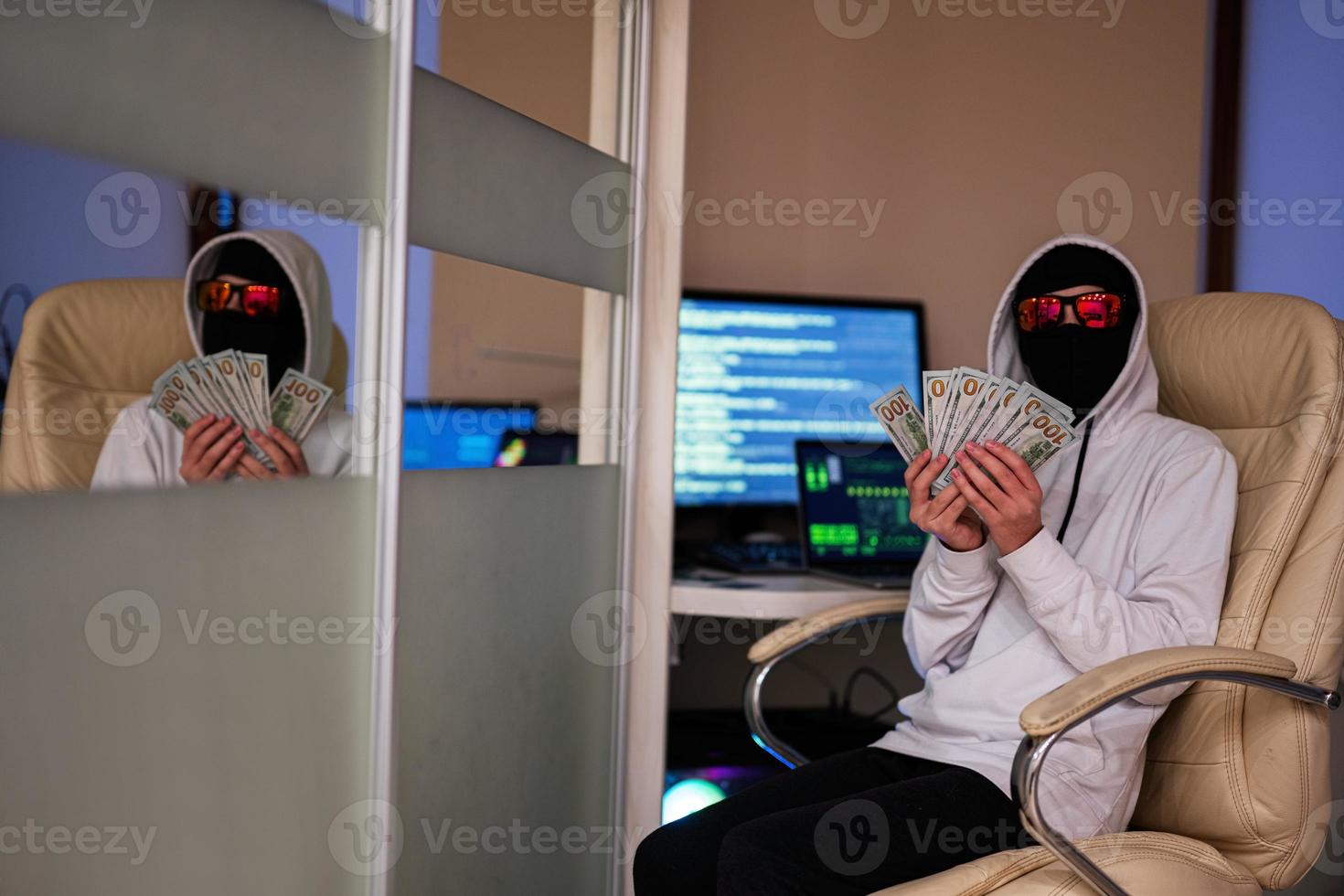 Boy hacker with money dollars. Internet theft . Man wearing a balaclava sat behind a laptop. photo