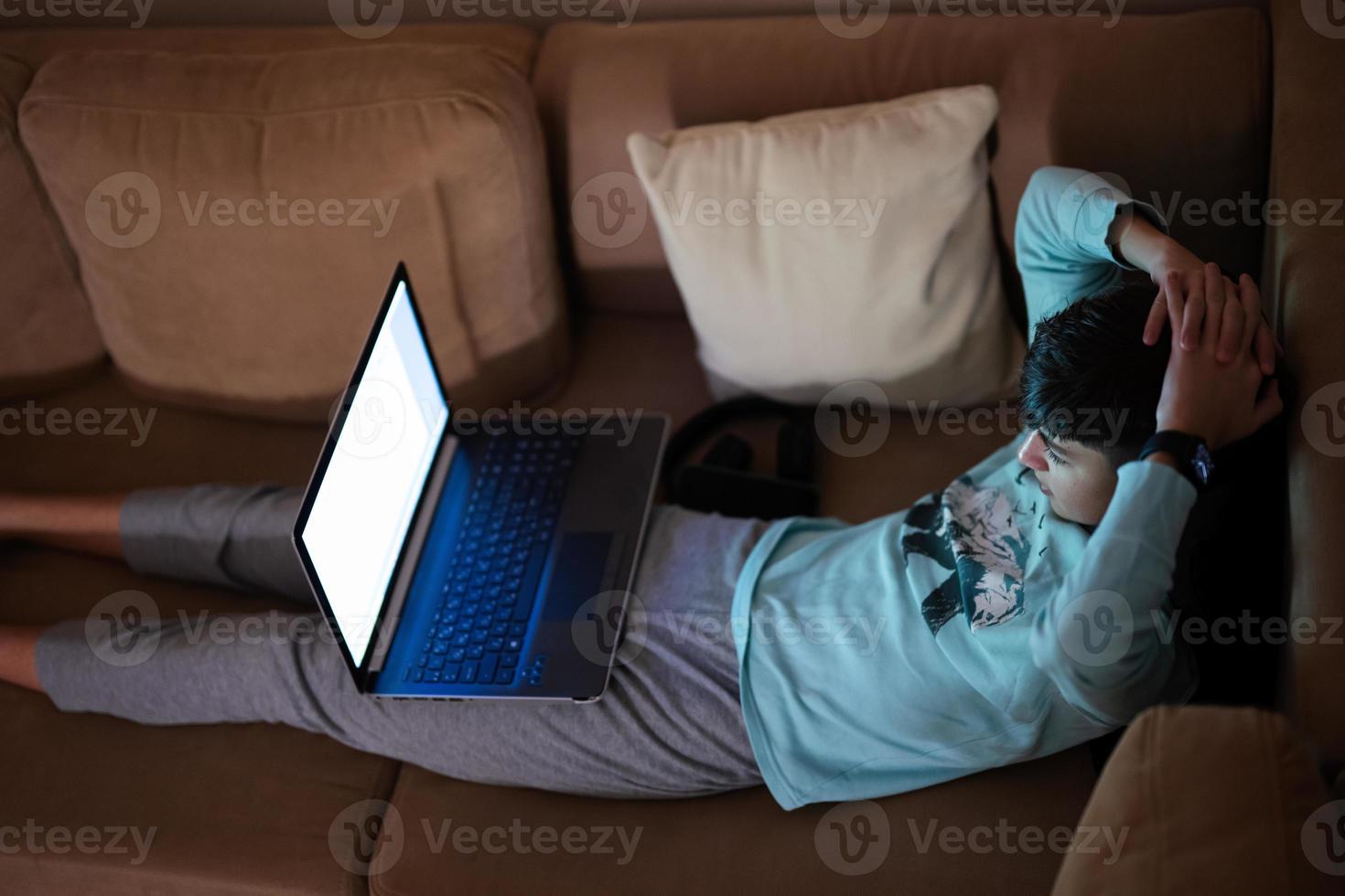 joven adolescente chico en frente de un ordenador portátil en un cama a noche acecho fútbol americano fósforo. foto