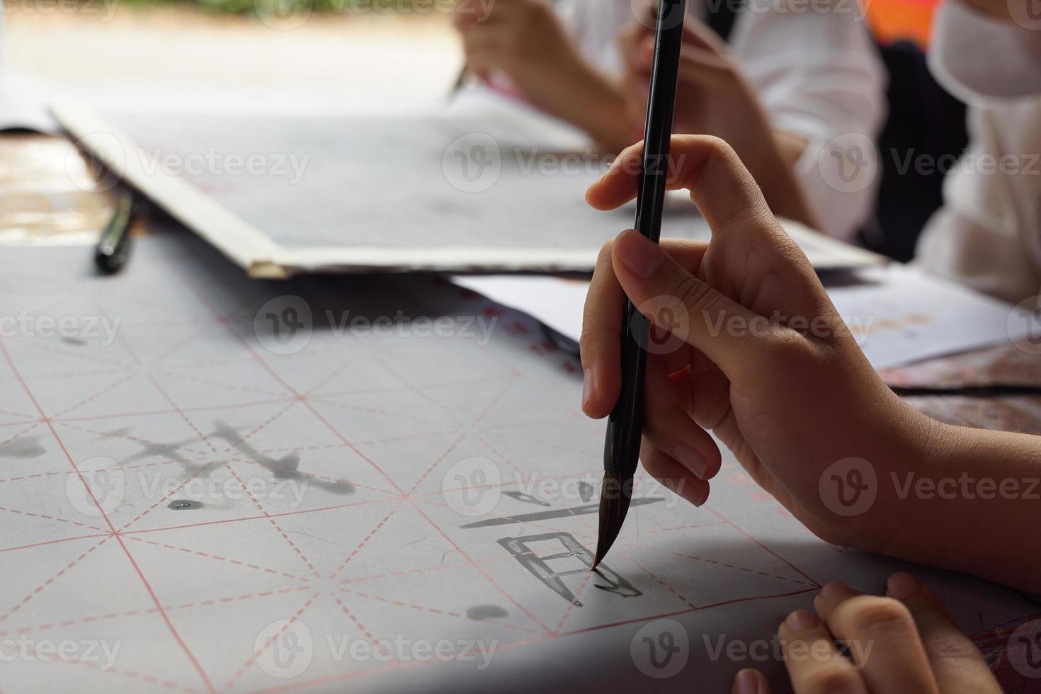 asiático estudiantes práctica el Arte de chino caligrafía por escritura chino caracteres en papel. suave y selectivo enfocar. foto