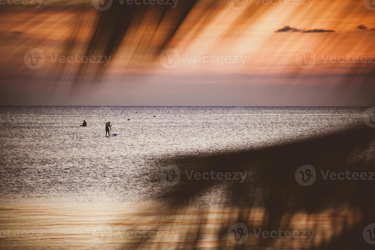 beautiful scene of vacation sea beach at sunset sky  looking through coconut leaves foreground photo