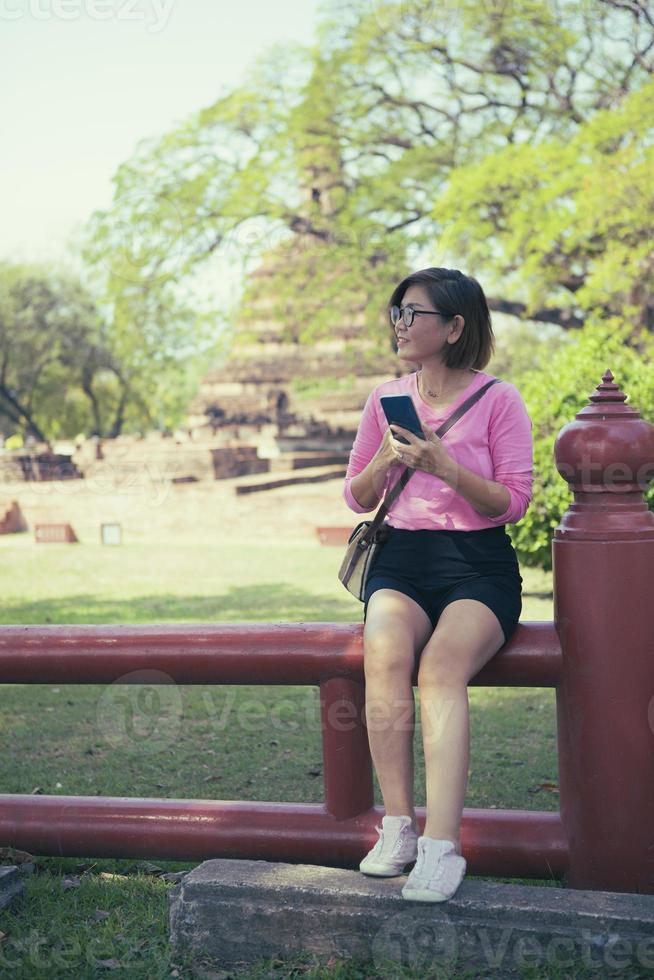 hermosa asiático mujer participación inteligente teléfono en mano y mirando a ligero mano con felicidad cara foto