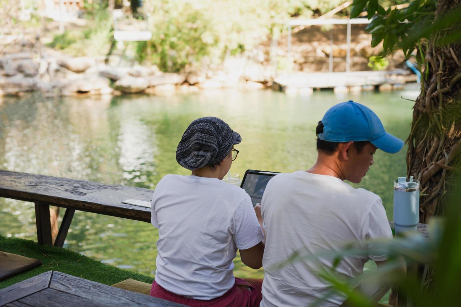 Couple working on laptop computer sitting on the floor outdoor with river in background. photo