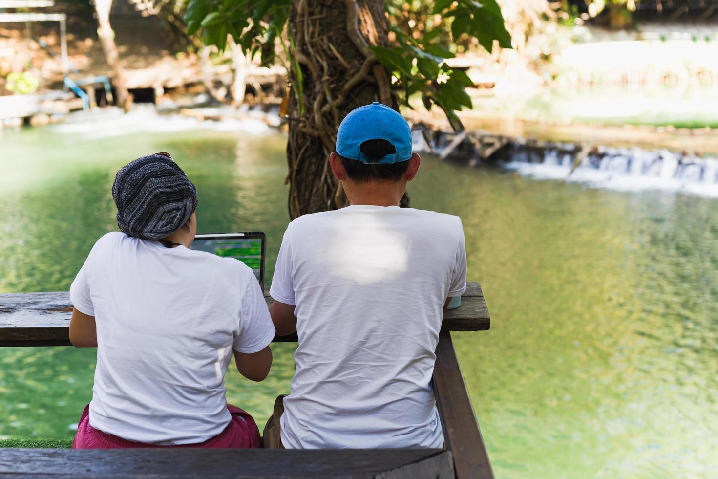 Couple working on laptop computer sitting on the floor outdoor with river in background. photo