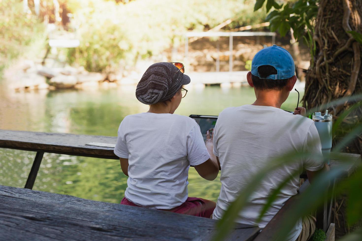 Couple working on laptop computer sitting on the floor outdoor with river in background. photo