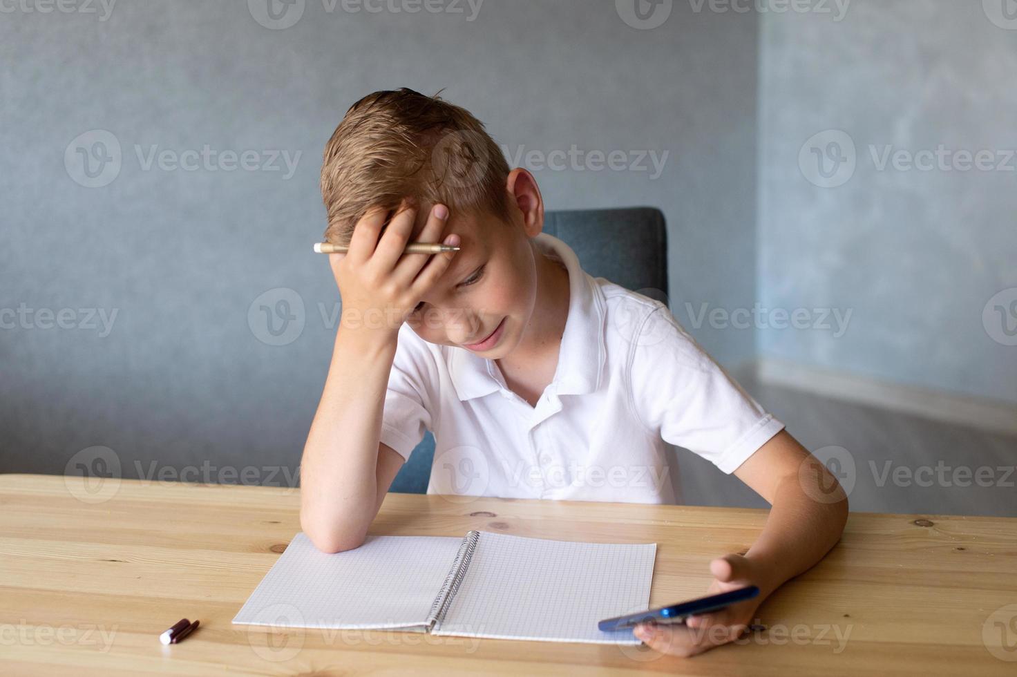 Cute boy writes in an open notebook and looks at the phone. photo