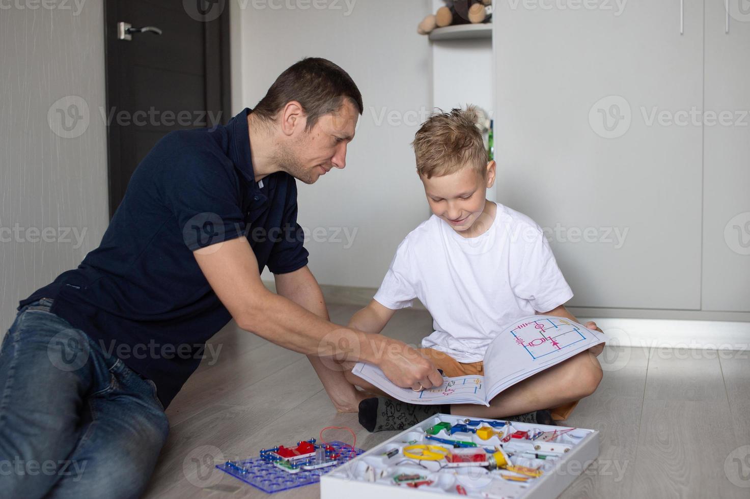 A cute boy in a white T-shirt collects an electrical designer with his dad in the room photo
