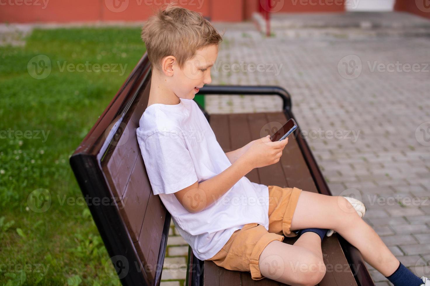 The boy is sitting on a bench and looking at the phone photo
