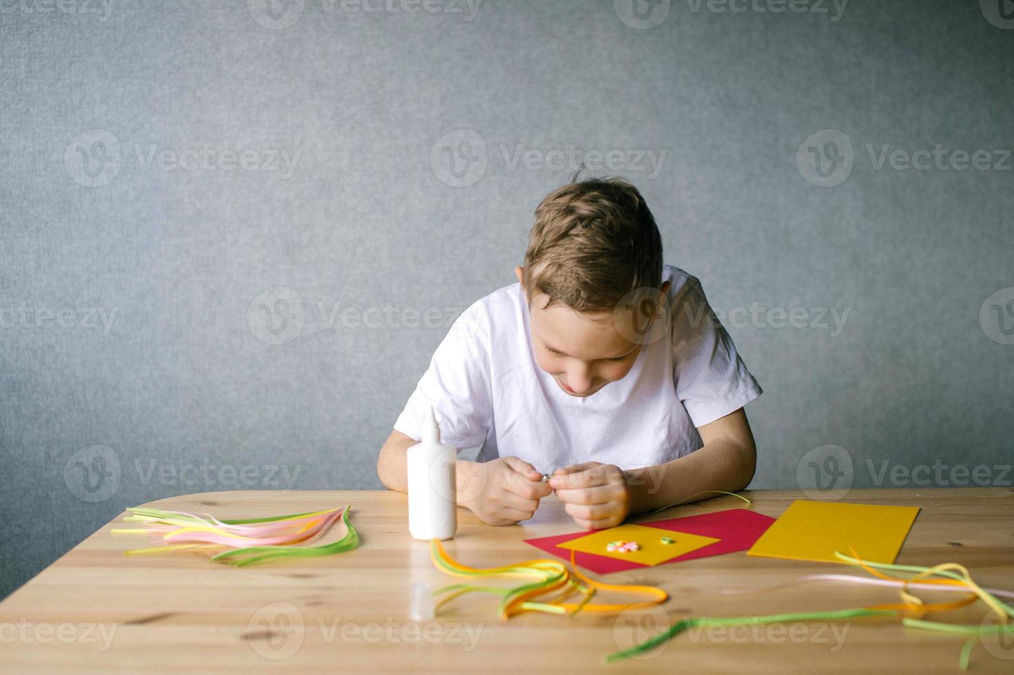 Cute boy makes flowers for a postcard by quilling while sitting at a table photo