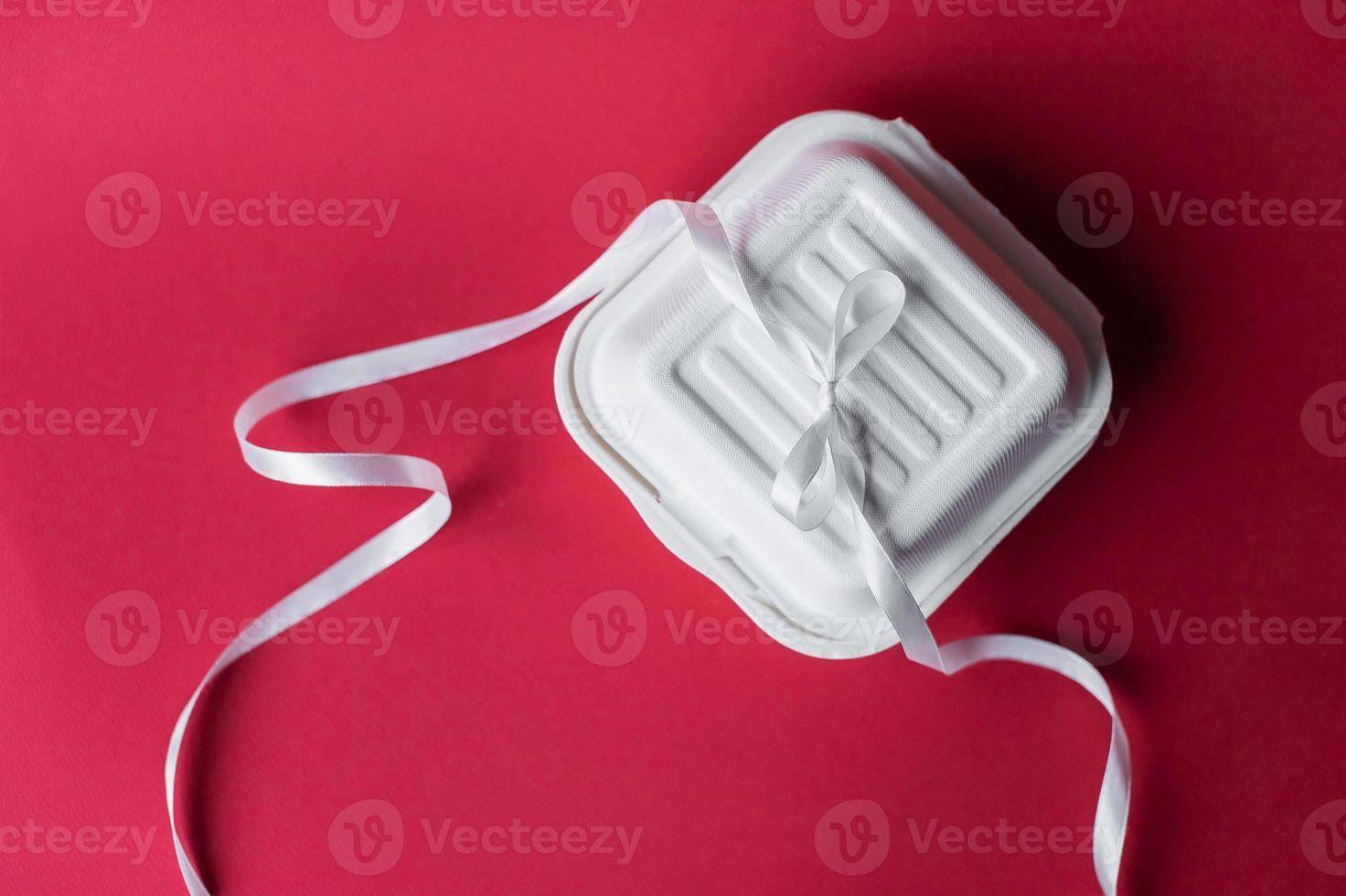Closed bento cake box on red background. White ribbon for gifts photo