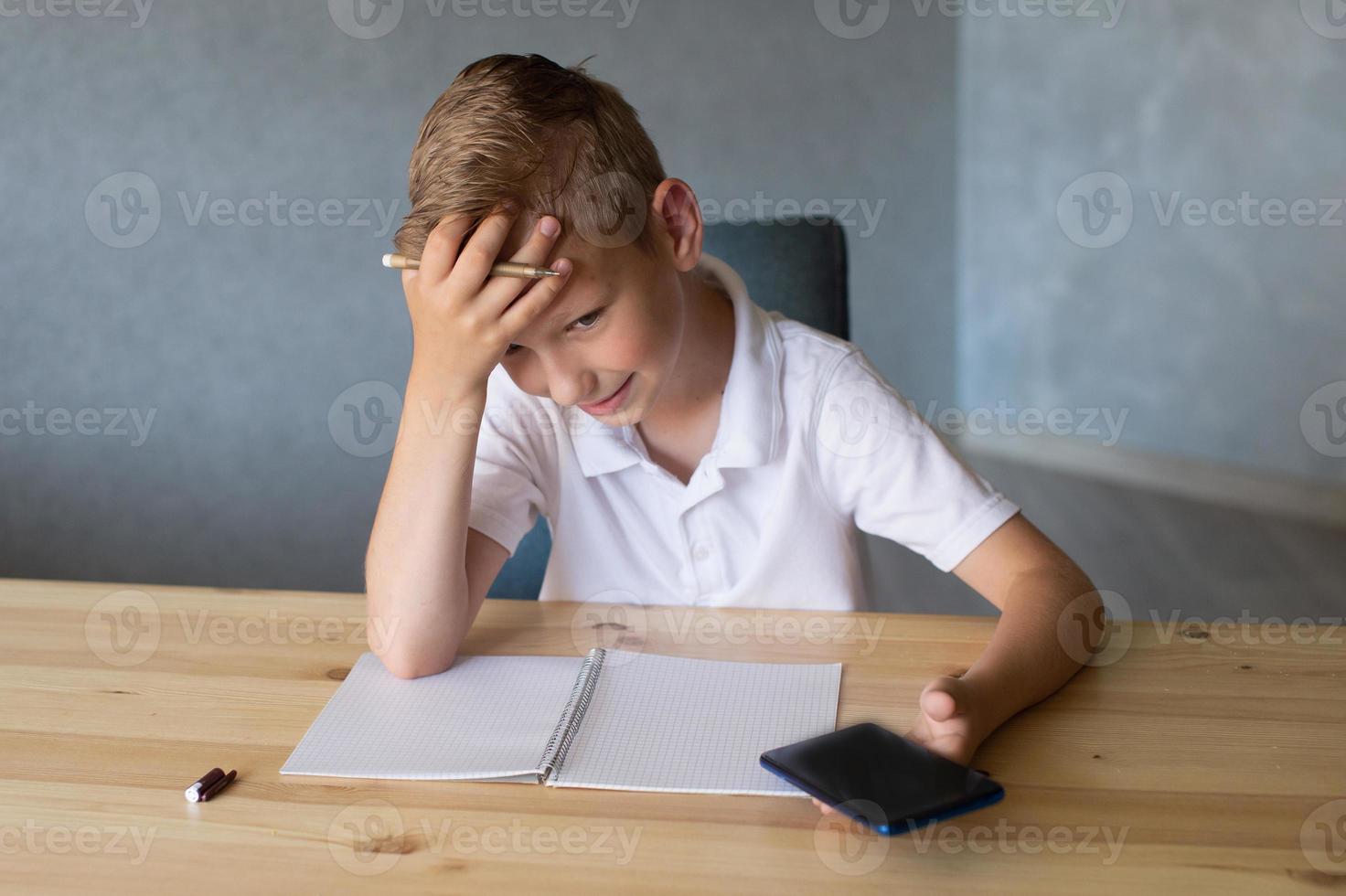 Cute boy writes in an open notebook and looks at the phone. photo