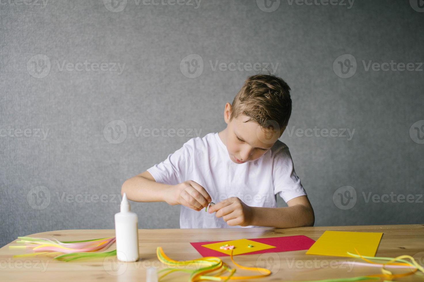 Cute boy makes flowers for a postcard by quilling while sitting at a table photo