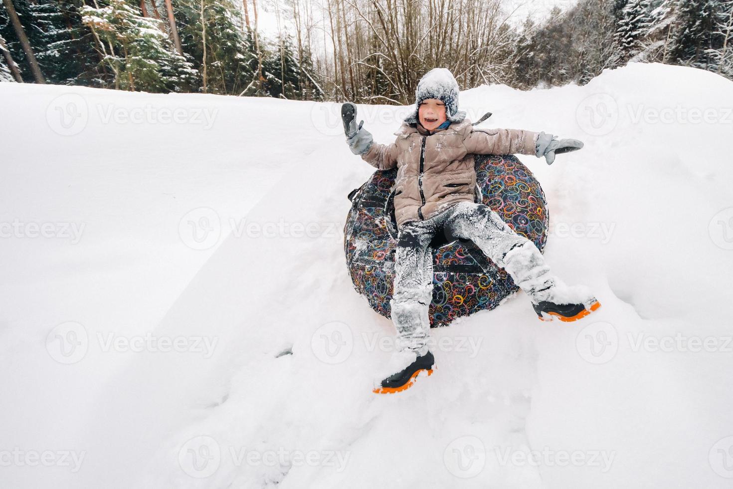 A boy is sitting in a tubing in the snow and riding down a slide photo