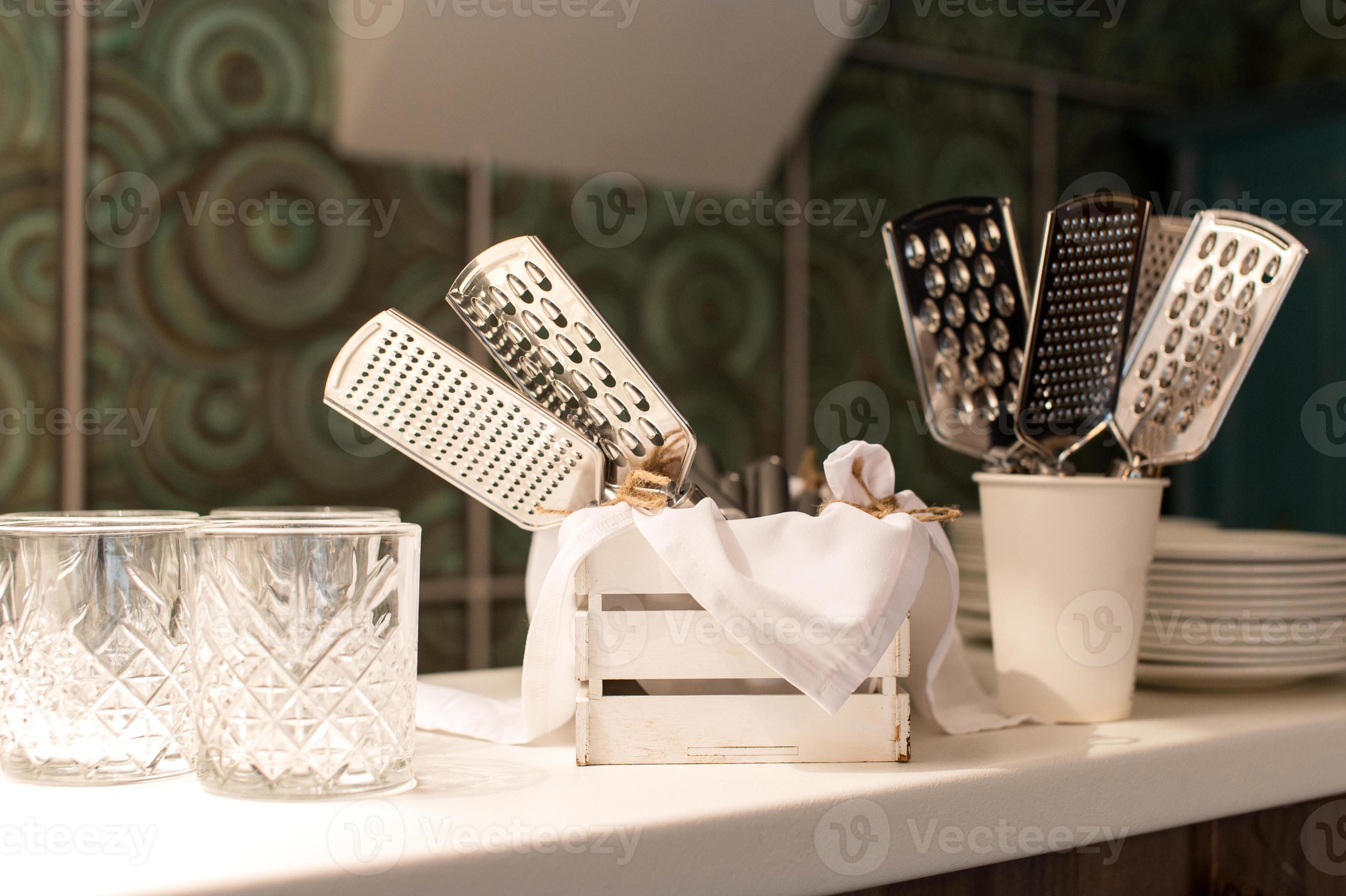 A set of hand graters stands near glasses and plates in the kitchen