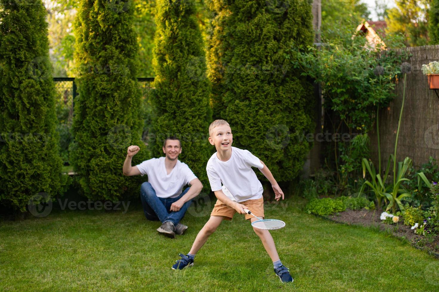 A cheerful dad on the street supports his son. A boy is playing badminton in a white T-shirt photo