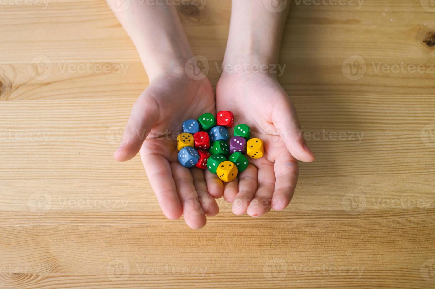 Child's hands hold a lot of multi-colored playing dice photo