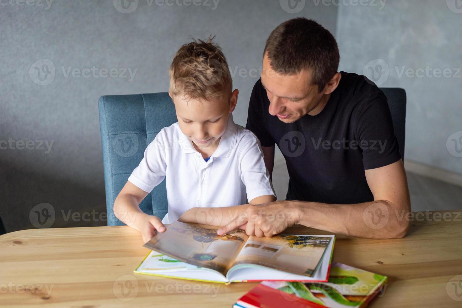 un linda chico es sentado a el mesa con su papá y acecho un libro acerca de serpientes foto