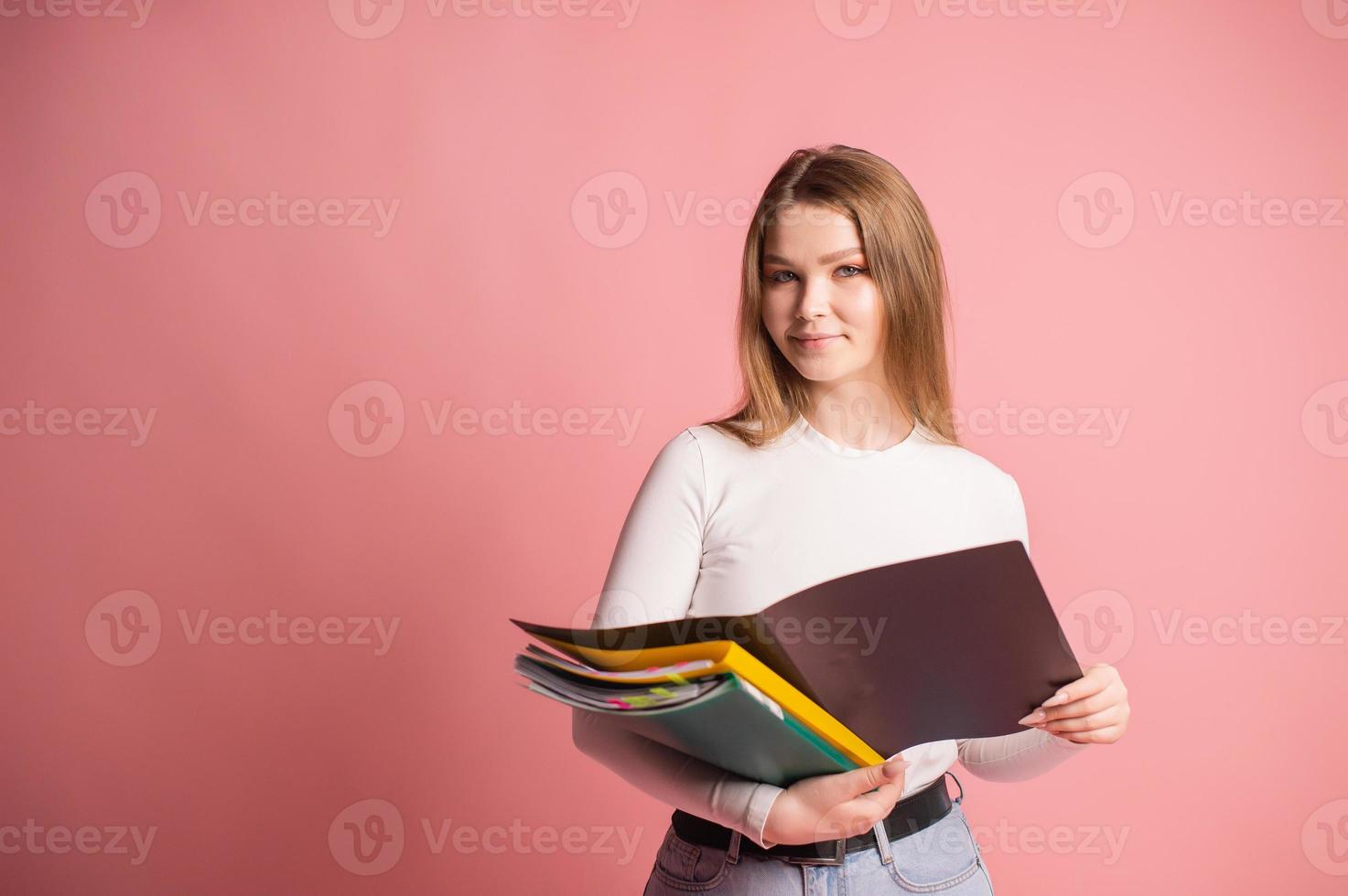 A cute student girl with a set of folders for documents stands on a pink background photo