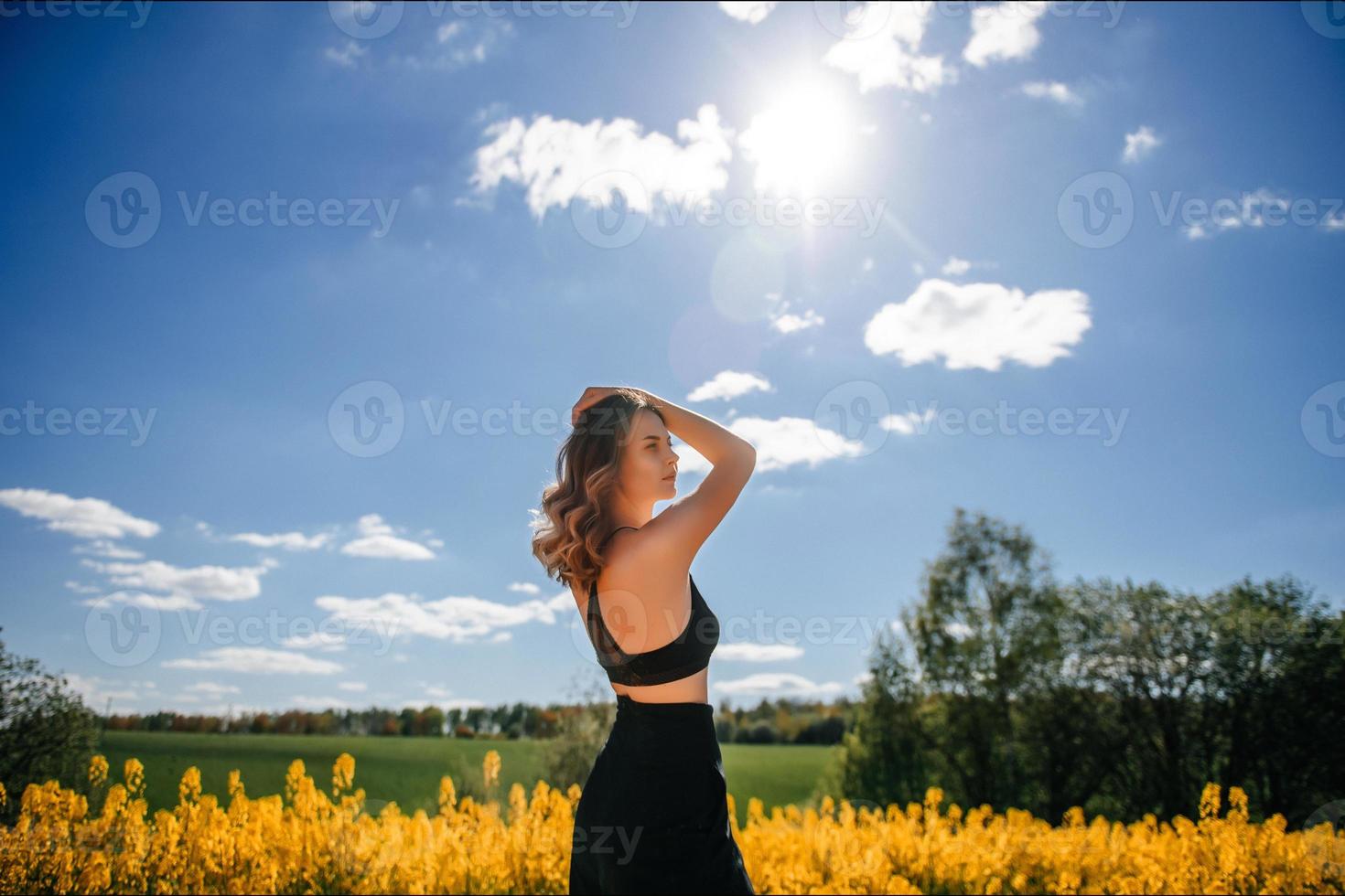 a girl in a black top and black trousers stands in a yellow rapeseed field in spring photo