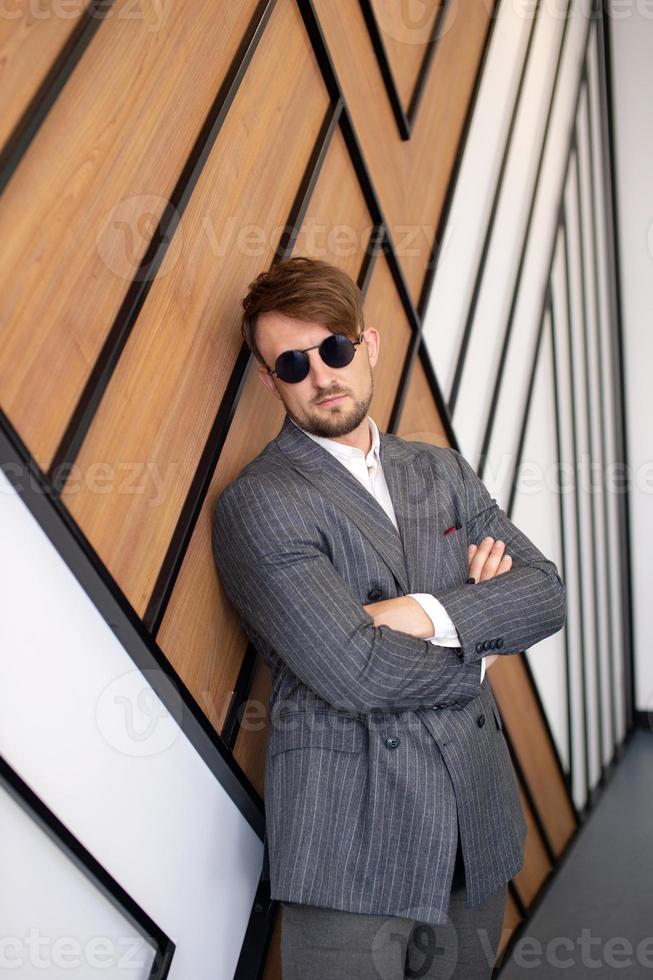 a young man in a suit and sunglasses is standing in a room near the wall photo
