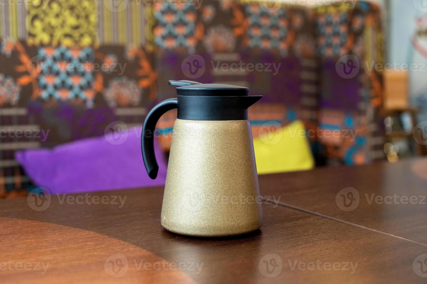 A golden teapot with a black lid stands on the table photo